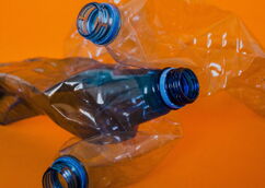 Three crushed plastic bottles with blue caps against an orange background
