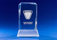 Crystal glass trophy with an engraved automotive logo and the inscription “MOST INNOVATIVE USE OF PLASTICS” on a blue background