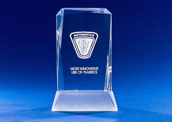 Kristallglas-Trophäe mit eingraviertem Automobil-Logo und der Aufschrift 'MOST INNOVATIVE USE OF PLASTICS' vor blauem Hintergrund