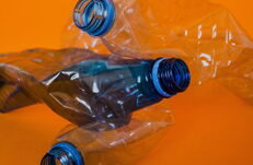 Drei zerdrückte Plastikflaschen mit blauen Verschlüssen vor orangefarbenem Hintergrund